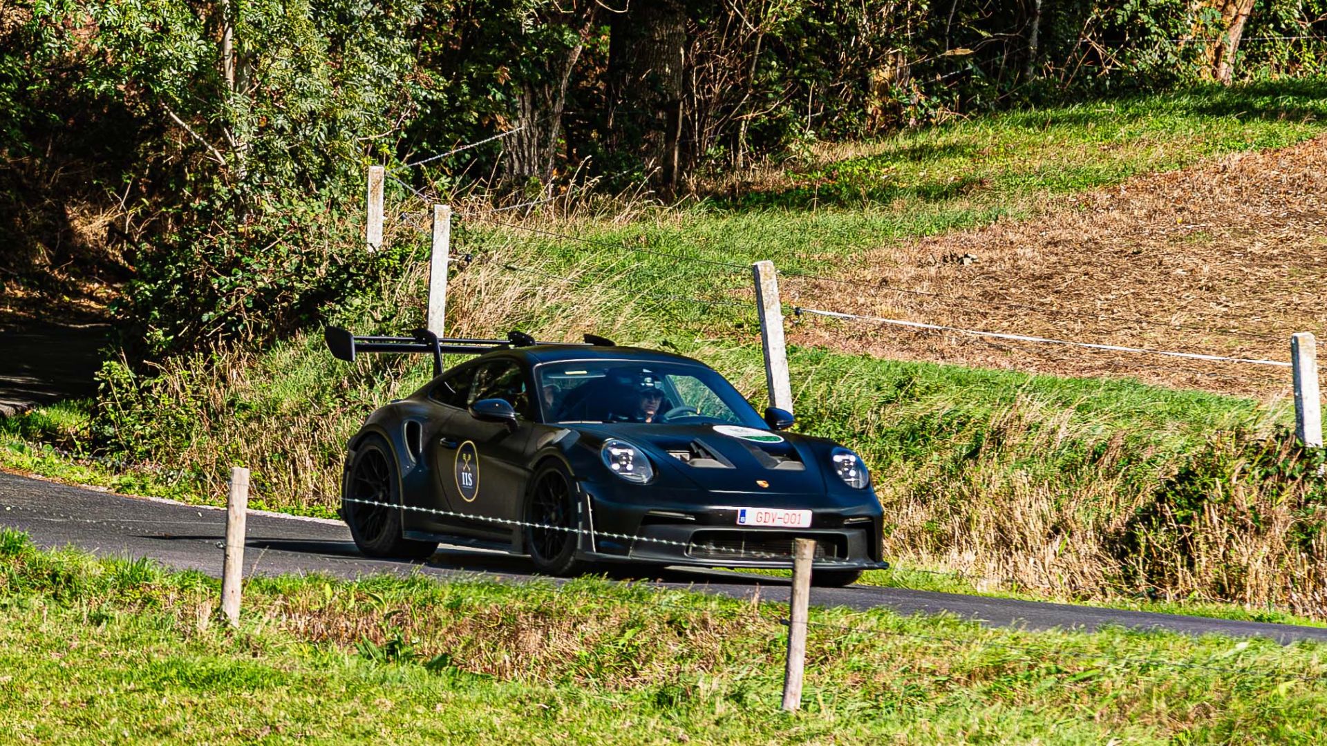 Zwarte Porsche op een landweg tussen de weilanden tijdens de Zoute GT Tour